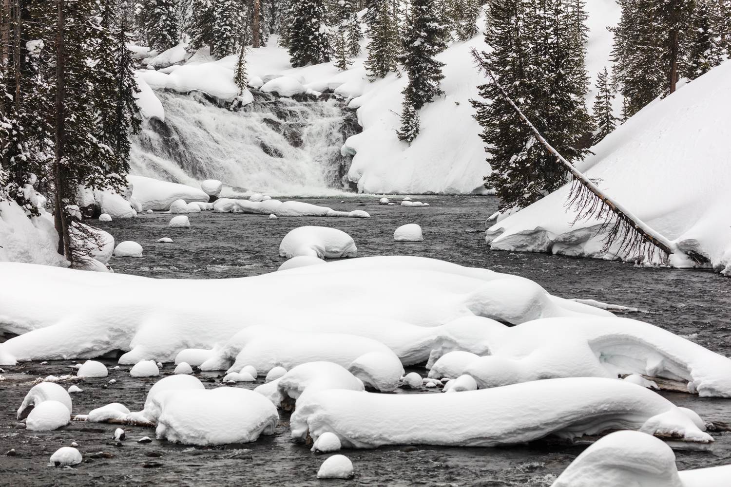 The Lewis River in winter with snow-capped rocks below the falls.