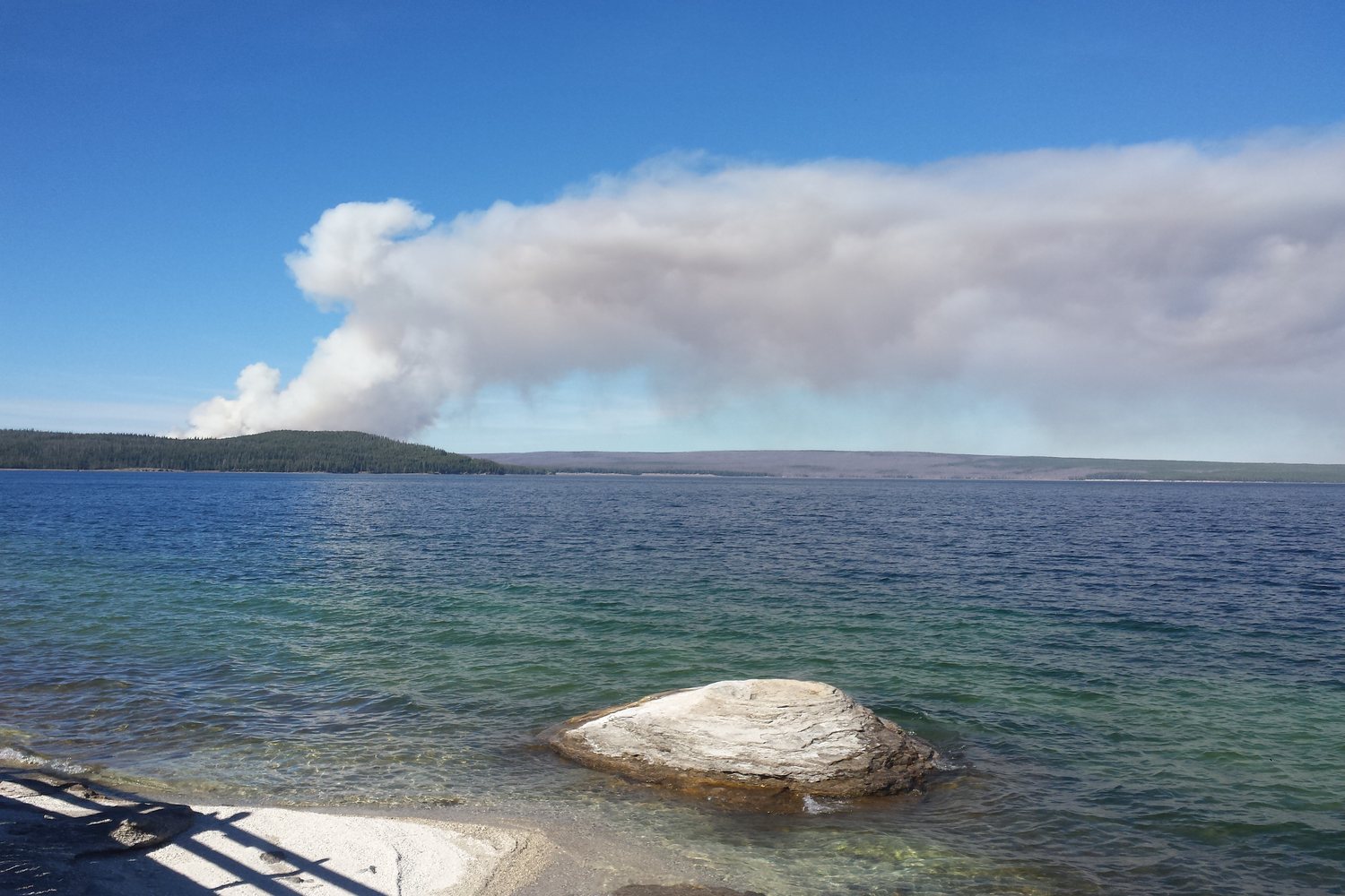 Yellowstone Lake from the West Thumb shore with a plume of smoke rising on the far side.